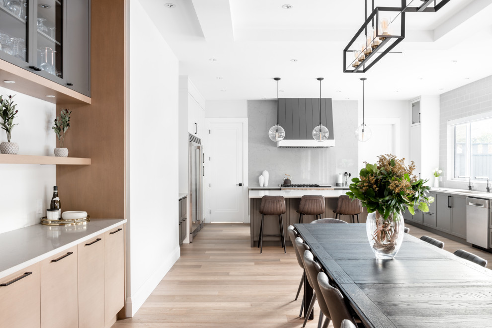 Eat-in kitchen - large transitional u-shaped medium tone wood floor and brown floor eat-in kitchen idea in Vancouver with an undermount sink, shaker cabinets, gray cabinets, quartz countertops, gray backsplash, stone slab backsplash, stainless steel appliances, an island and gray countertops
