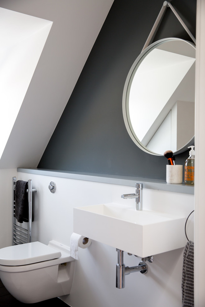 Photo of a large contemporary bathroom in London with recessed-panel cabinets, a shower/bathtub combo, a wall-mount toilet, white walls, ceramic floors, a wall-mount sink and black floor.