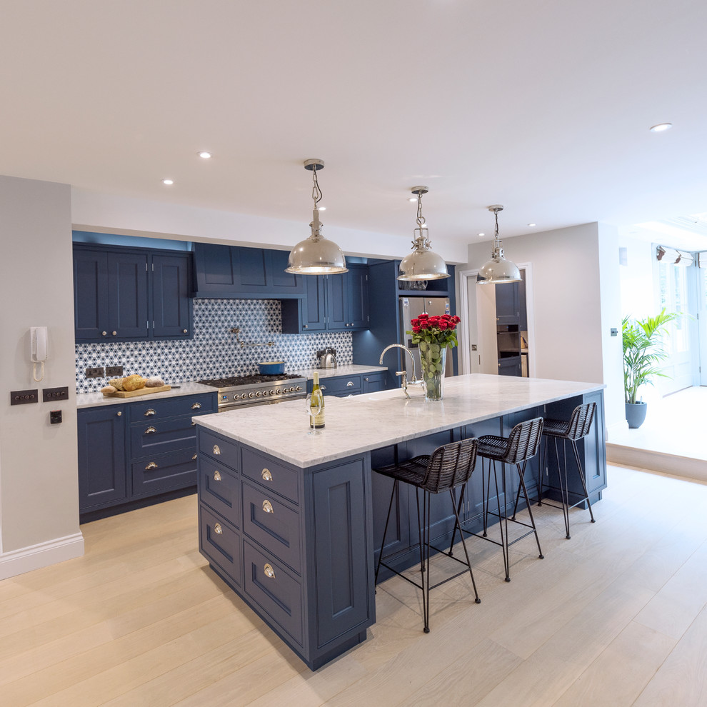 Photo of a large modern galley open plan kitchen in Other with a farmhouse sink, recessed-panel cabinets, blue cabinets, marble benchtops, blue splashback, stainless steel appliances, light hardwood floors, with island, beige floor and beige benchtop.