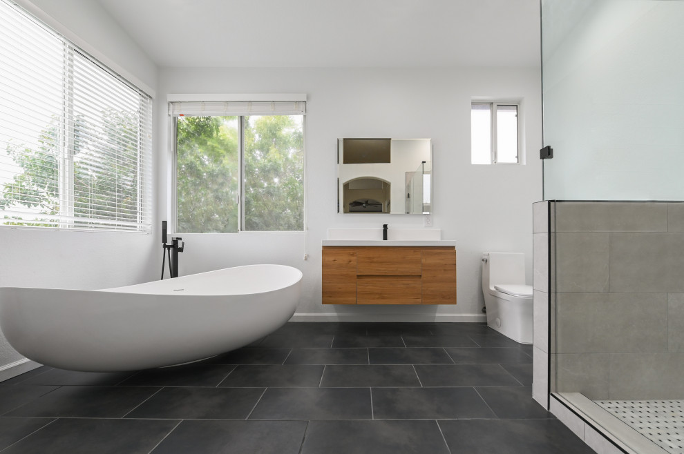 Photo of a mid-sized modern master bathroom in Austin with flat-panel cabinets, medium wood cabinets, a freestanding tub, a double shower, a one-piece toilet, white walls, ceramic floors, a drop-in sink, marble benchtops, black floor, a hinged shower door, white benchtops, a single vanity and a floating vanity.