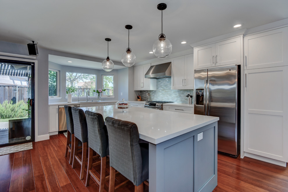 Photo of a mid-sized arts and crafts l-shaped eat-in kitchen in San Francisco with an undermount sink, white cabinets, blue splashback, glass tile splashback, stainless steel appliances, dark hardwood floors, with island, brown floor, recessed-panel cabinets and granite benchtops.