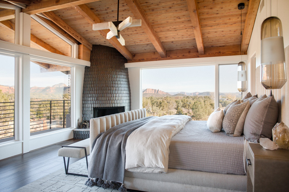 Uriges Hauptschlafzimmer mit weißer Wandfarbe, dunklem Holzboden, Eckkamin, gefliester Kaminumrandung, schwarzem Boden, freigelegten Dachbalken und gewölbter Decke in Phoenix