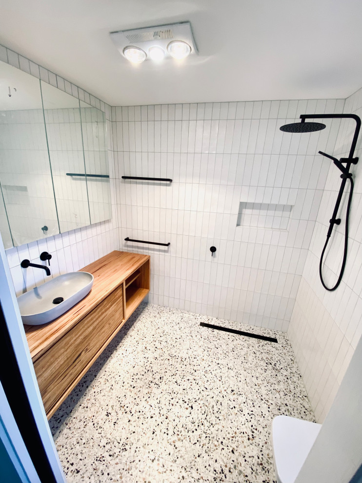 Photo of a small contemporary bathroom in Other with furniture-like cabinets, medium wood cabinets, an open shower, a one-piece toilet, white tile, ceramic tile, white walls, terrazzo floors, a vessel sink, wood benchtops, an open shower, brown benchtops, a single vanity and a floating vanity.
