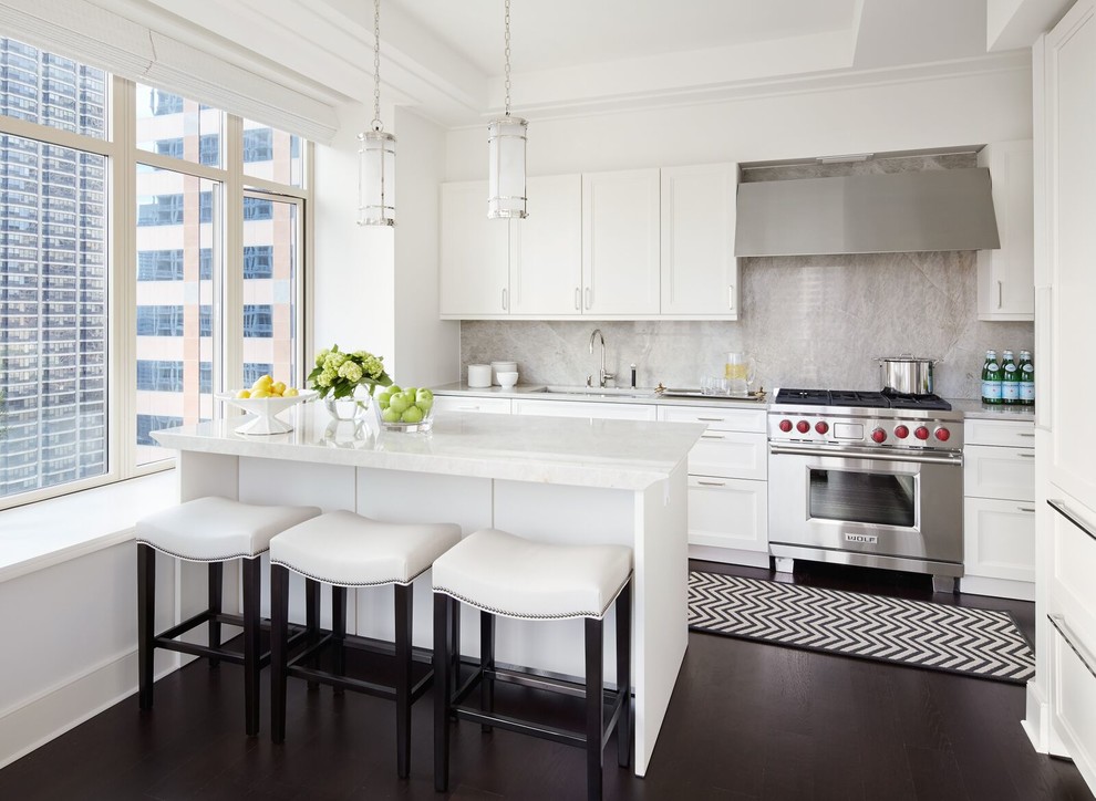 Example of a transitional dark wood floor kitchen design in New York with an undermount sink, recessed-panel cabinets, white cabinets, beige backsplash, stainless steel appliances and an island