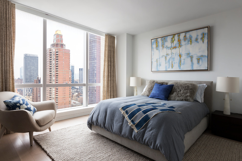 This is an example of a transitional guest bedroom in New York with white walls, light hardwood floors and beige floor.