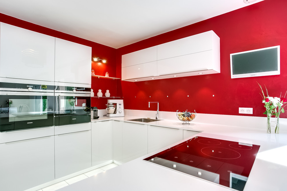 Contemporary u-shaped eat-in kitchen in Paris with an undermount sink, flat-panel cabinets, white cabinets, red splashback and white appliances.
