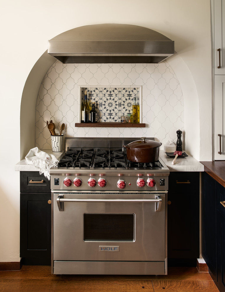 Inspiration for a mid-sized mediterranean u-shaped eat-in kitchen in San Francisco with recessed-panel cabinets, black cabinets, marble benchtops, a peninsula, a farmhouse sink, white splashback, porcelain splashback, stainless steel appliances, medium hardwood floors, brown floor and white benchtop.