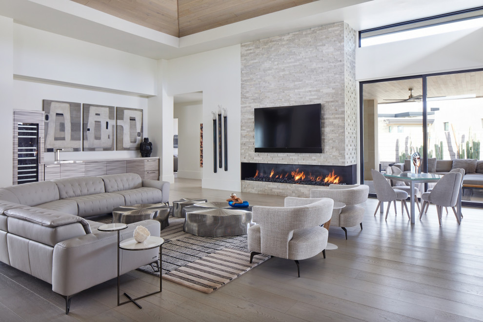 Inspiration for a large contemporary open plan games room in Phoenix with a home bar, white walls, medium hardwood flooring, a ribbon fireplace, a stacked stone fireplace surround, a wall mounted tv, brown floors, a drop ceiling and a chimney breast.