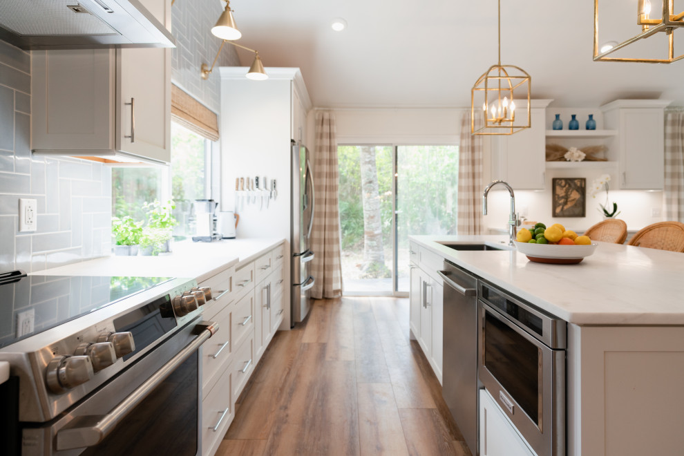 Design ideas for a large beach style open plan kitchen in Charleston with a single-bowl sink, shaker cabinets, white cabinets, marble benchtops, blue splashback, ceramic splashback, stainless steel appliances, with island, brown floor, white benchtop and vaulted.