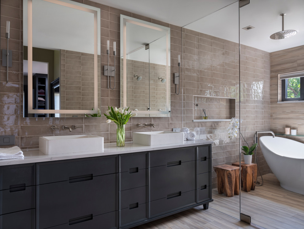 This is an example of a mid-sized transitional master wet room bathroom in Denver with grey cabinets, a freestanding tub, a one-piece toilet, beige tile, porcelain tile, porcelain floors, a vessel sink, engineered quartz benchtops, beige floor, a hinged shower door, white benchtops and flat-panel cabinets.