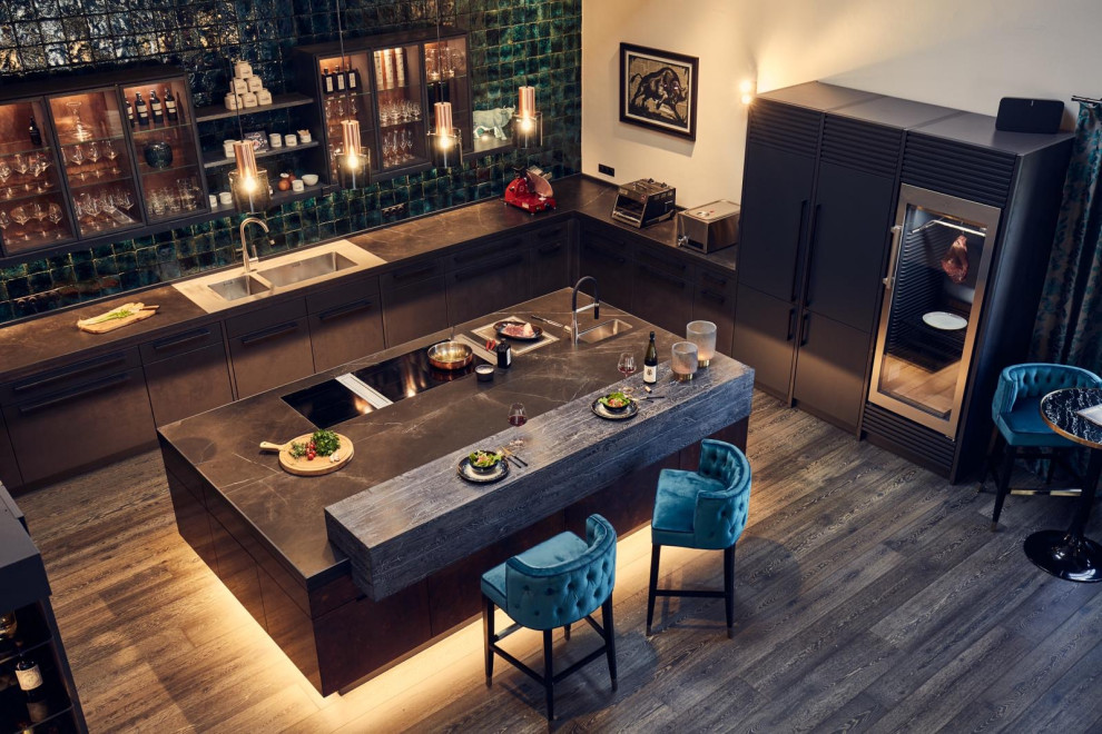 This is an example of a large industrial u-shaped open plan kitchen in Munich with an undermount sink, flat-panel cabinets, tile benchtops, green splashback, subway tile splashback, dark hardwood floors, with island, black benchtop and exposed beam.