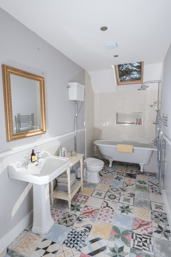 Photo of a mid-sized traditional kids bathroom in Cork with a claw-foot tub, a shower/bathtub combo, a two-piece toilet, multi-coloured tile, porcelain tile, grey walls, porcelain floors and a pedestal sink.