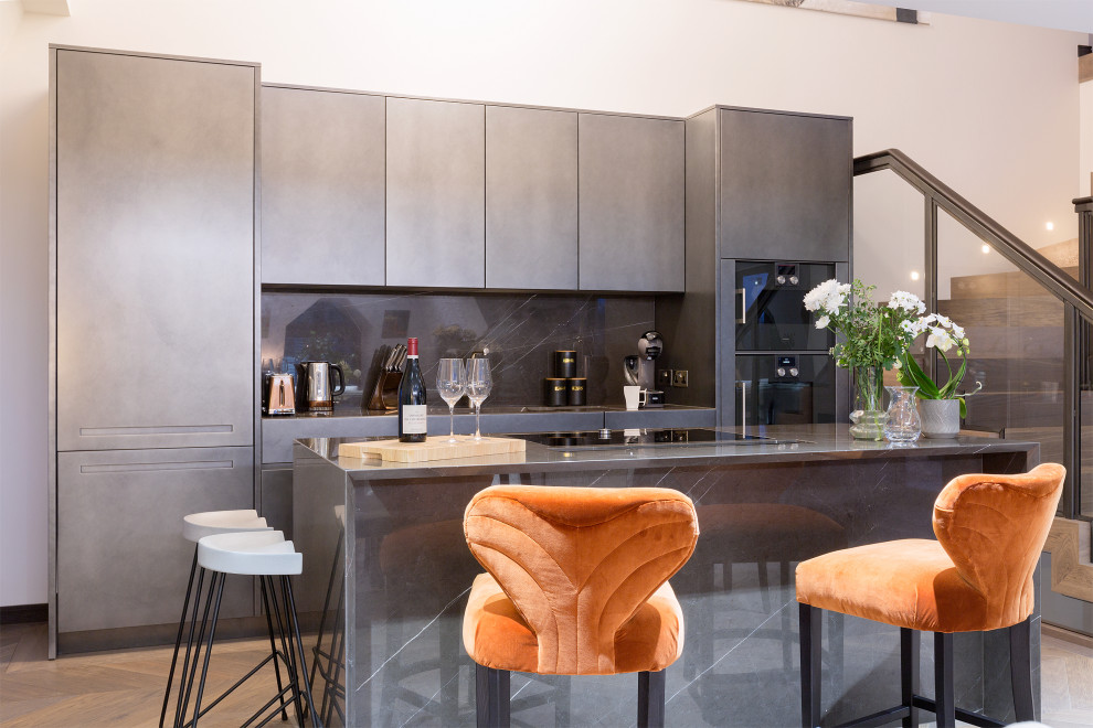 Zweizeilige Moderne Küche mit flächenbündigen Schrankfronten, grauen Schränken, Küchenrückwand in Schwarz, Rückwand aus Stein, Elektrogeräten mit Frontblende, braunem Holzboden, Kücheninsel, braunem Boden und grauer Arbeitsplatte in London