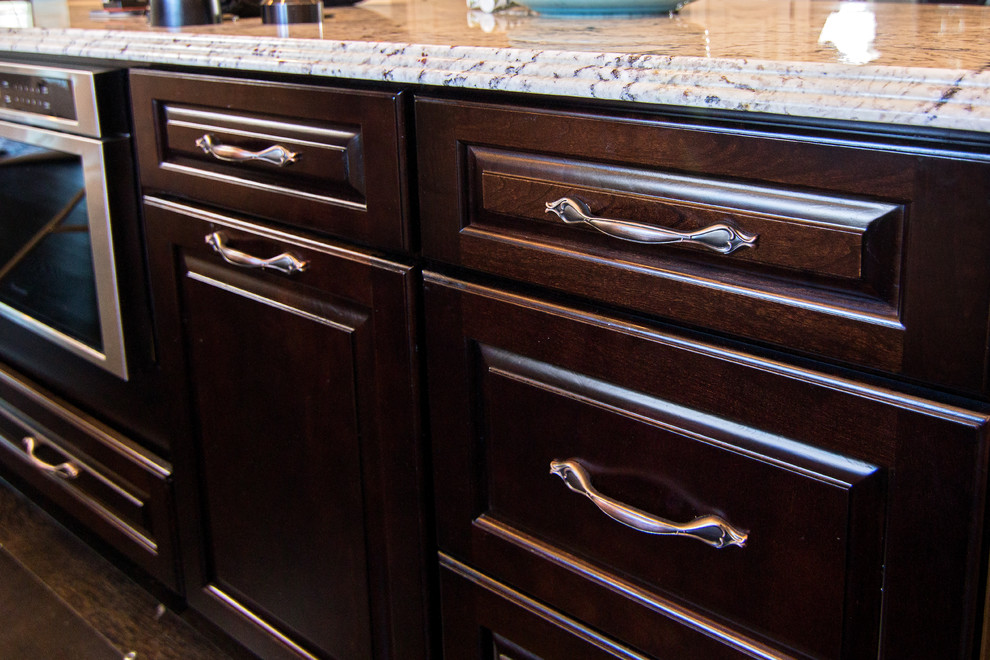 Transitional l-shaped dark wood floor kitchen photo in Providence with a farmhouse sink, raised-panel cabinets, granite countertops, gray backsplash, glass tile backsplash, paneled appliances and an island