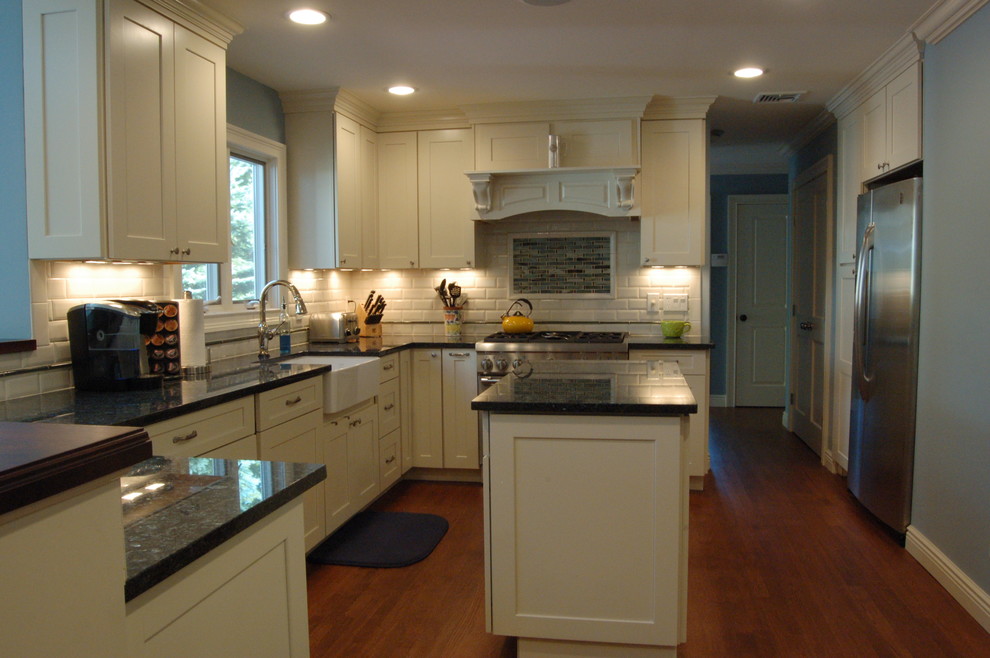 This is an example of a traditional u-shaped eat-in kitchen in New York with a farmhouse sink, shaker cabinets, yellow cabinets, granite benchtops, white splashback, porcelain splashback and stainless steel appliances.