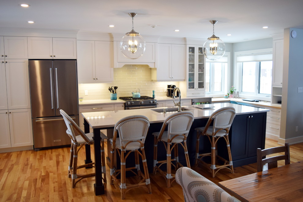 Example of a large transitional l-shaped light wood floor open concept kitchen design in Ottawa with an undermount sink, shaker cabinets, white cabinets, quartz countertops, white backsplash, subway tile backsplash, stainless steel appliances and an island