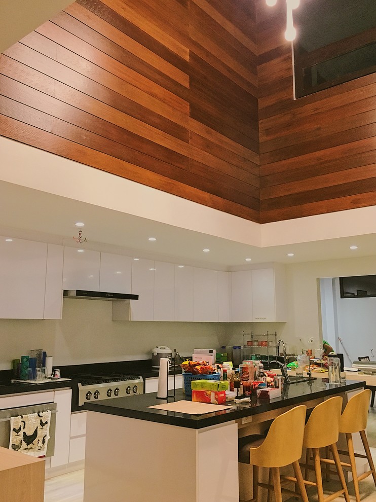 Example of a transitional kitchen pantry design with white cabinets, solid surface countertops, white backsplash, glass sheet backsplash, an island and black countertops