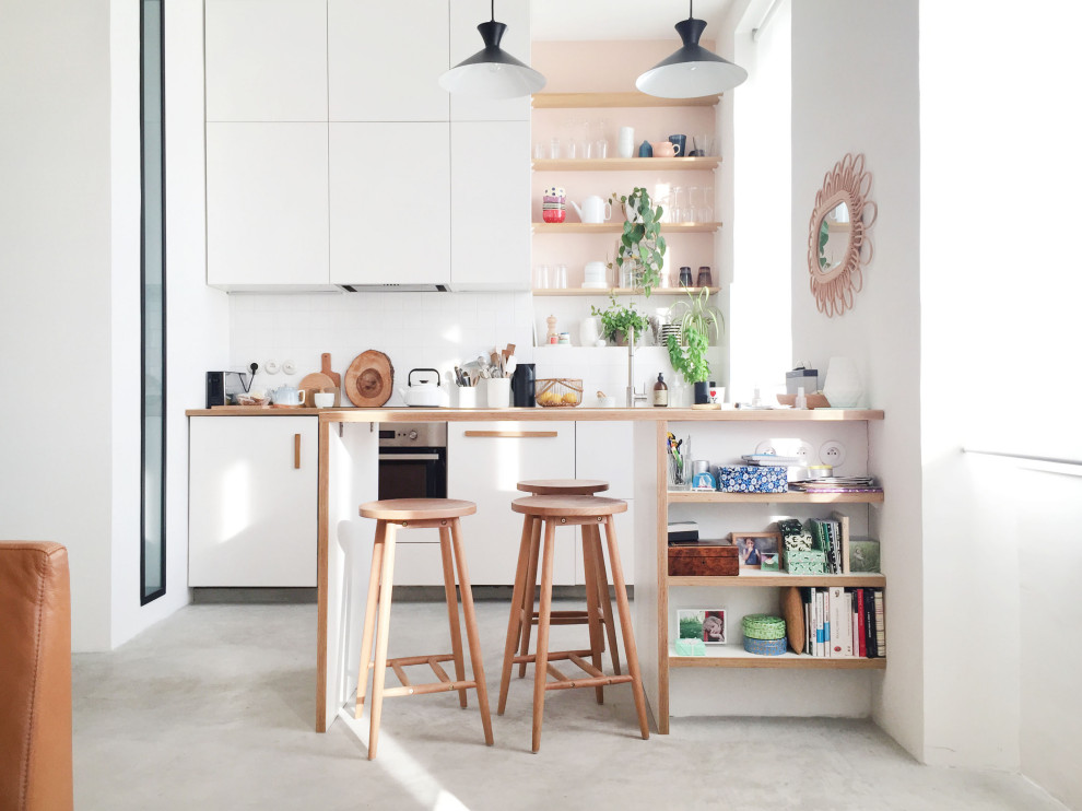 This is an example of a small contemporary galley kitchen in Marseille with flat-panel cabinets, white cabinets, wood benchtops, white splashback, panelled appliances, a peninsula, grey floor and beige benchtop.