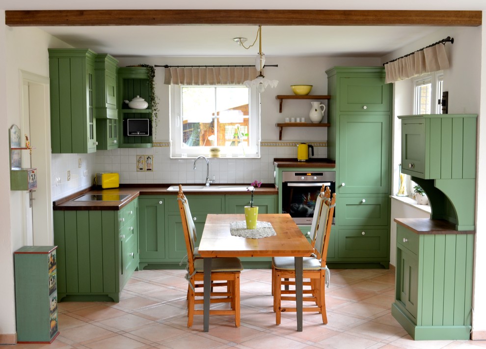 Inspiration for a large country eat-in kitchen in Berlin with a drop-in sink, green cabinets, white splashback, stainless steel appliances, shaker cabinets, wood benchtops, subway tile splashback and no island.