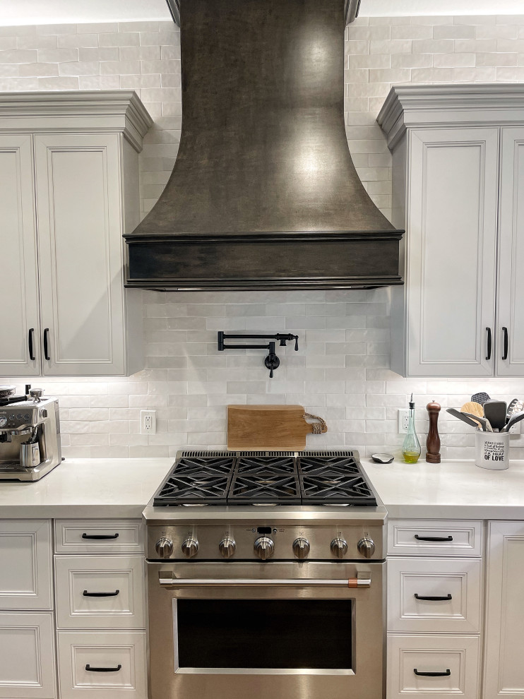 Exempel på ett mellanstort klassiskt vit vitt kök, med en undermonterad diskho, luckor med infälld panel, vita skåp, bänkskiva i kvarts, vitt stänkskydd, stänkskydd i tunnelbanekakel, rostfria vitvaror, laminatgolv, en köksö och beiget golv