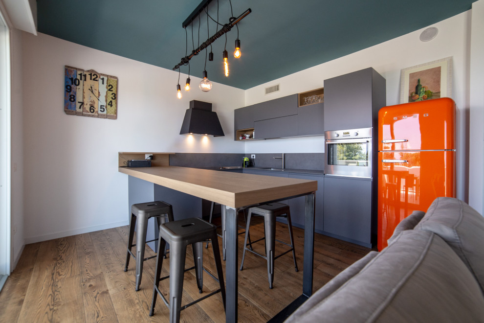 Industrial u-shaped open plan kitchen in Other with an undermount sink, flat-panel cabinets, grey cabinets, coloured appliances, dark hardwood floors, a peninsula, brown floor and grey benchtop.