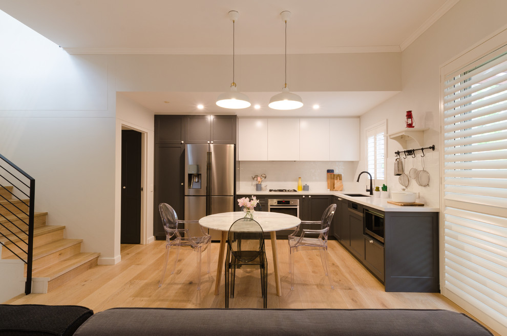 This is an example of a mid-sized contemporary l-shaped eat-in kitchen in Sydney with a drop-in sink, shaker cabinets, grey cabinets, quartz benchtops, white splashback, subway tile splashback, stainless steel appliances, light hardwood floors and no island.