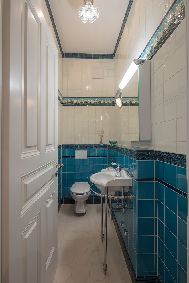 This is an example of a small traditional powder room in Munich with a two-piece toilet, blue tile, white tile, glass tile, ceramic floors, a wall-mount sink, solid surface benchtops and white floor.