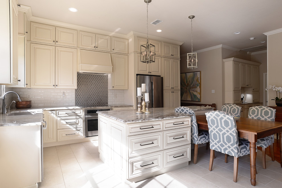 Mid-sized traditional l-shaped open plan kitchen in Dallas with raised-panel cabinets, beige cabinets, white splashback, subway tile splashback, stainless steel appliances, with island and beige floor.