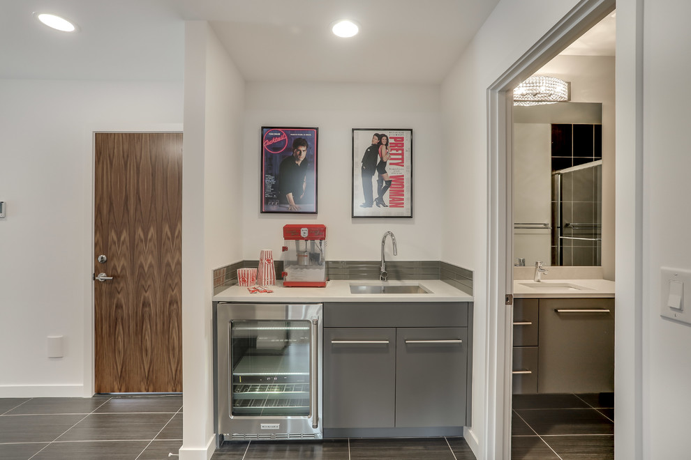 Large contemporary galley wet bar in Seattle with an undermount sink, flat-panel cabinets, grey cabinets, solid surface benchtops, grey splashback, glass tile splashback, ceramic floors and grey floor.