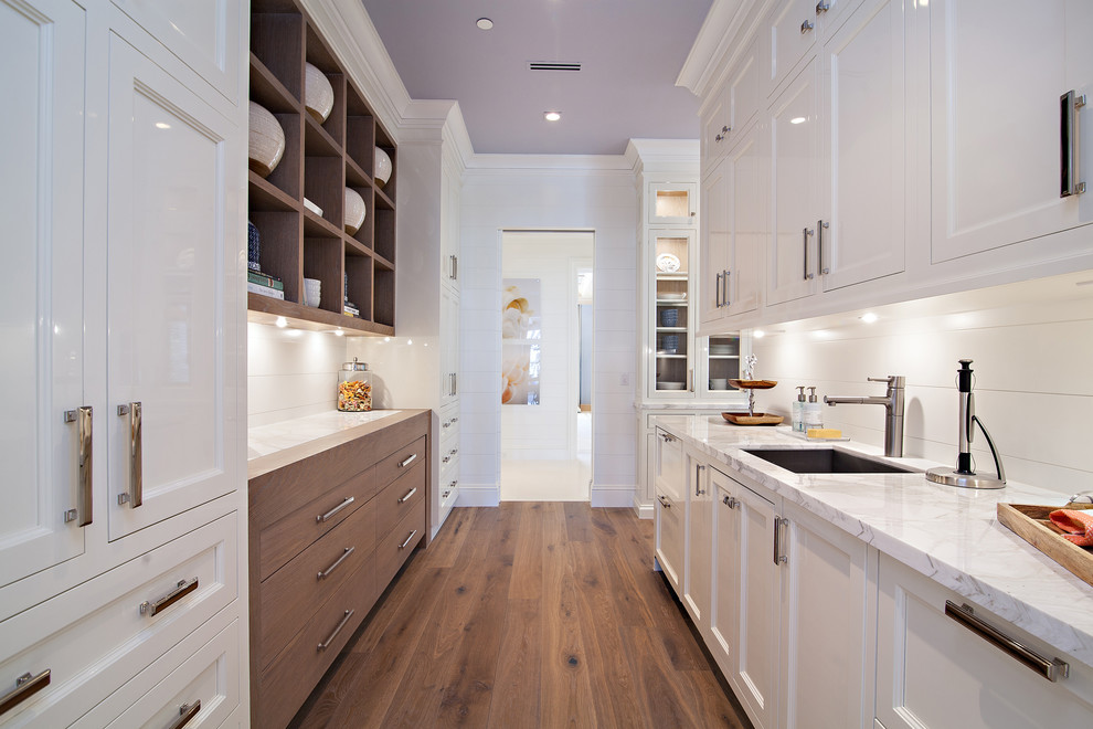 Design ideas for an expansive transitional kitchen pantry in Miami with an undermount sink, shaker cabinets, white cabinets, marble benchtops, white splashback, stone slab splashback, white appliances, medium hardwood floors and with island.