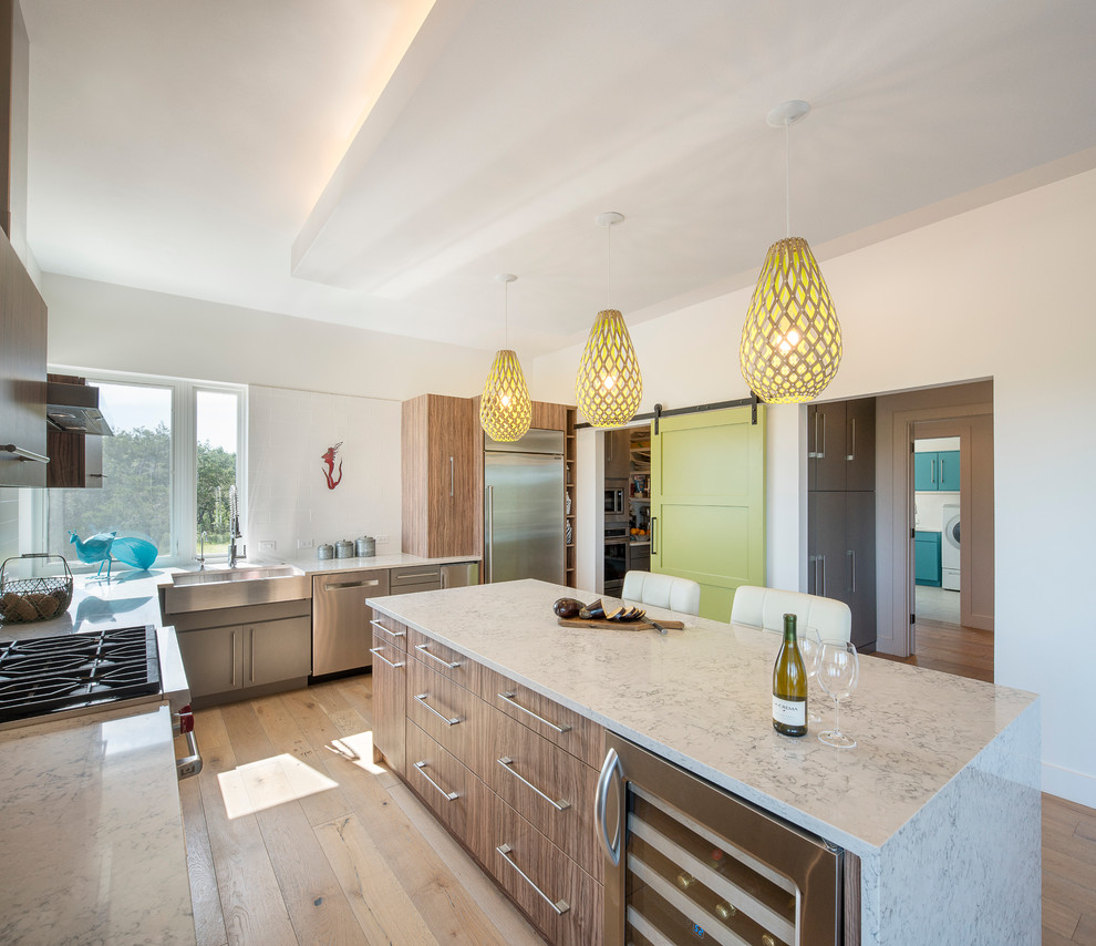 Example of a mid-sized minimalist l-shaped light wood floor eat-in kitchen design in Austin with a farmhouse sink, flat-panel cabinets, light wood cabinets, quartz countertops, white backsplash, stainless steel appliances and an island