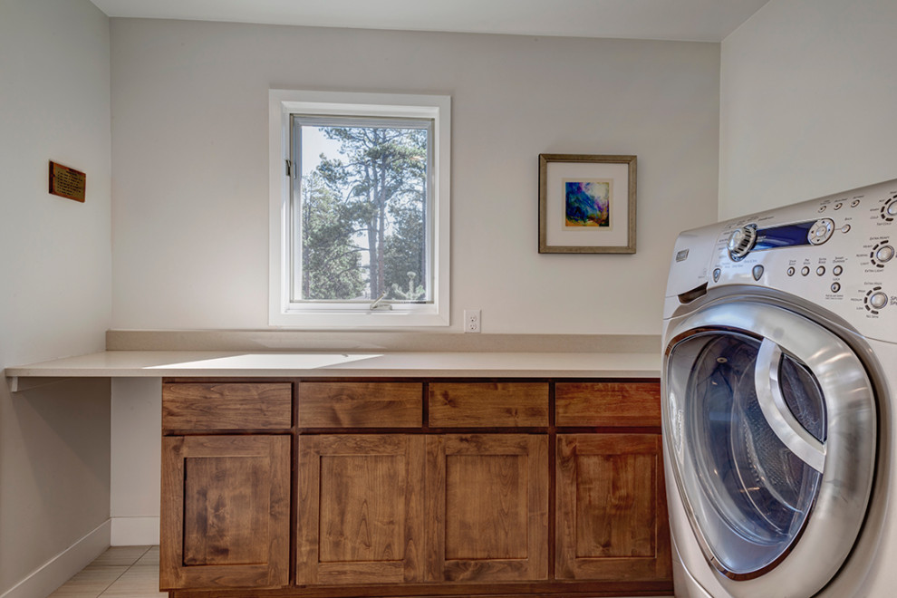 Mid-sized midcentury l-shaped dedicated laundry room in Denver with flat-panel cabinets, medium wood cabinets, granite benchtops, beige walls, ceramic floors, a stacked washer and dryer, beige floor and beige benchtop.