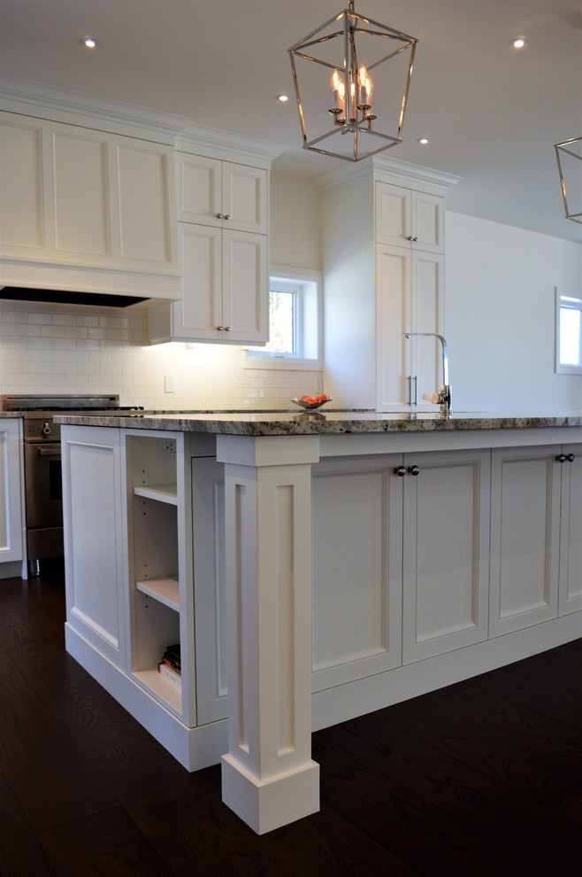 Expansive traditional l-shaped eat-in kitchen in Toronto with an undermount sink, shaker cabinets, white cabinets, granite benchtops, white splashback, ceramic splashback, stainless steel appliances, dark hardwood floors, with island, brown floor and multi-coloured benchtop.