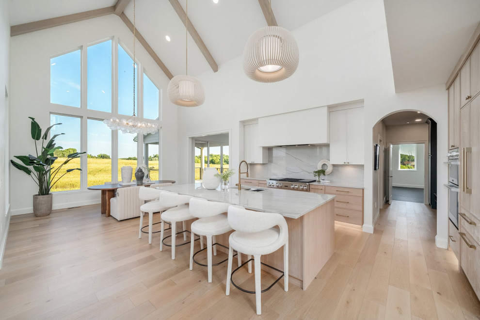 Inspiration for a large transitional l-shaped light wood floor, beige floor and vaulted ceiling eat-in kitchen remodel with an undermount sink, recessed-panel cabinets, light wood cabinets, quartzite countertops, white backsplash, granite backsplash, stainless steel appliances, an island and white countertops