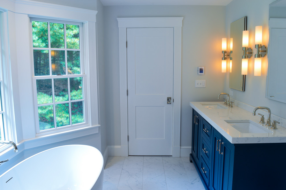 This is an example of a mid-sized traditional master bathroom in Boston with recessed-panel cabinets, blue cabinets, a freestanding tub, a curbless shower, a one-piece toilet, black and white tile, ceramic tile, ceramic floors, an undermount sink, engineered quartz benchtops, white floor, a hinged shower door and white benchtops.