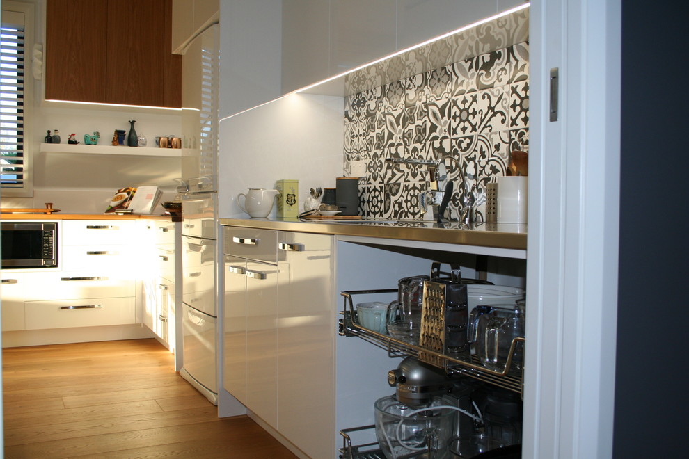 Contemporary galley kitchen pantry in Christchurch with stainless steel benchtops, grey splashback, ceramic splashback, light hardwood floors and brown floor.