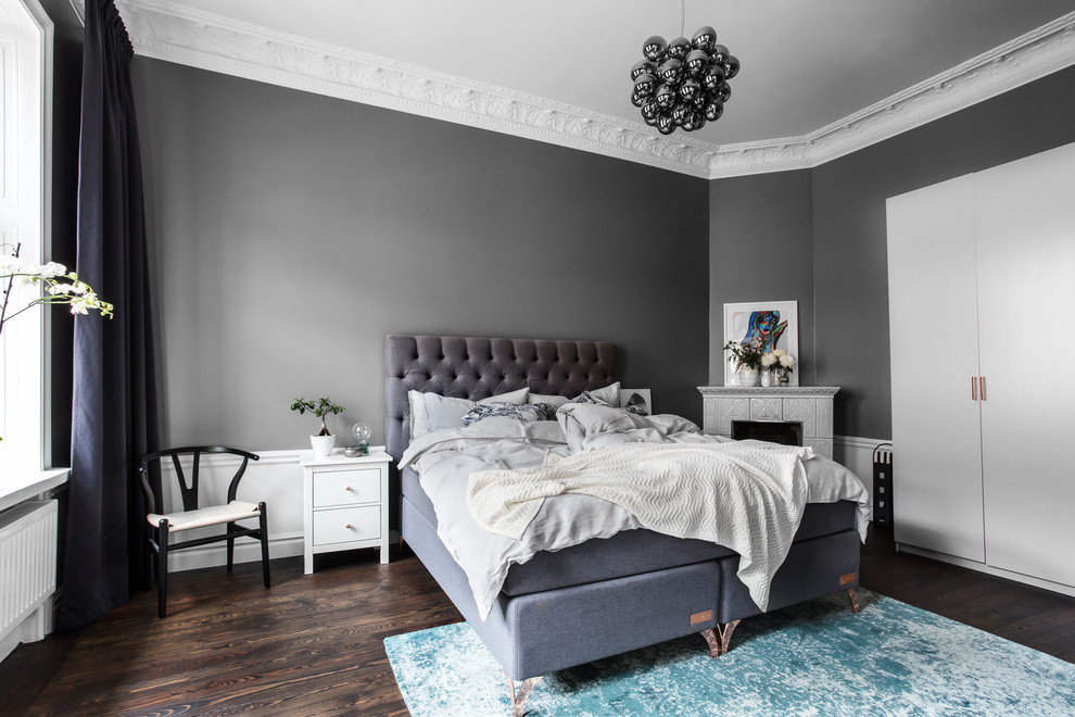 Scandinavian master bedroom in Stockholm with grey walls, dark hardwood floors, a corner fireplace, a tile fireplace surround and brown floor.