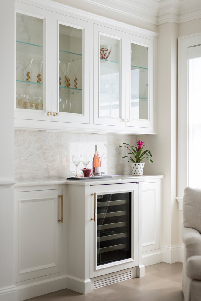 This is an example of a traditional single-wall home bar in Minneapolis with no sink, glass-front cabinets, white cabinets, white splashback, white benchtop and marble splashback.