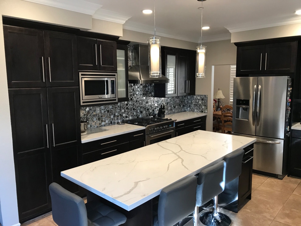 Photo of a mid-sized eclectic l-shaped eat-in kitchen in Los Angeles with a double-bowl sink, shaker cabinets, dark wood cabinets, quartz benchtops, metallic splashback, metal splashback, stainless steel appliances, porcelain floors, with island, beige floor and white benchtop.