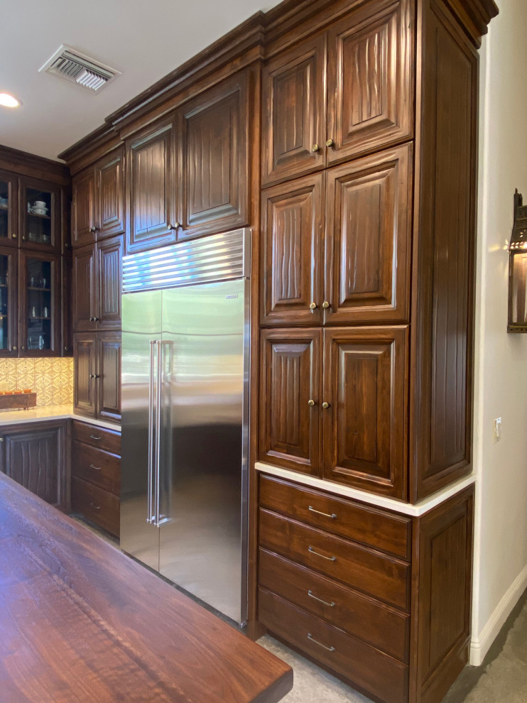 Example of a mid-sized mountain style u-shaped concrete floor and gray floor eat-in kitchen design in Phoenix with a farmhouse sink, raised-panel cabinets, distressed cabinets, wood countertops, multicolored backsplash, ceramic backsplash, stainless steel appliances, an island and brown countertops