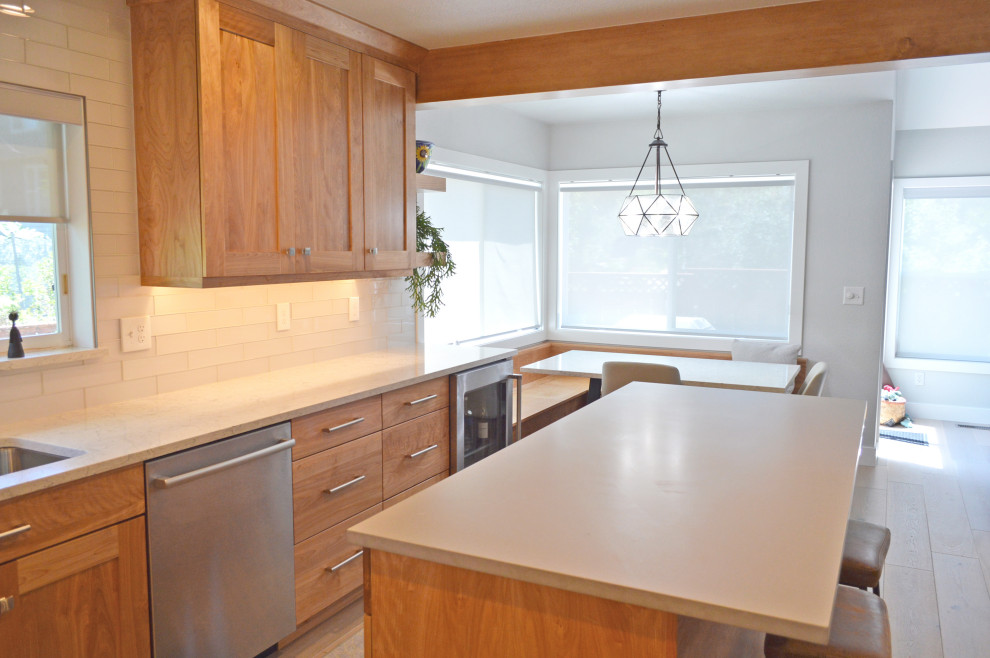 Mid-sized transitional u-shaped light wood floor, gray floor and exposed beam eat-in kitchen photo in Denver with an undermount sink, shaker cabinets, medium tone wood cabinets, quartz countertops, white backsplash, glass tile backsplash, stainless steel appliances, an island and multicolored countertops