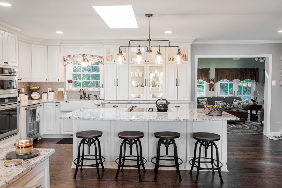 Photo of an expansive country u-shaped kitchen in Baltimore with a farmhouse sink, white cabinets, granite benchtops, brown floor, raised-panel cabinets, stainless steel appliances, dark hardwood floors, with island and white benchtop.