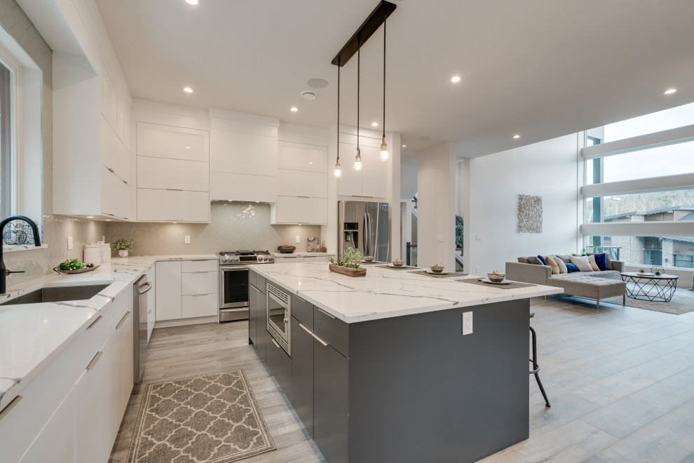 Photo of a mid-sized contemporary l-shaped eat-in kitchen in Vancouver with a single-bowl sink, flat-panel cabinets, white cabinets, quartzite benchtops, beige splashback, subway tile splashback, stainless steel appliances, laminate floors, with island, grey floor and white benchtop.