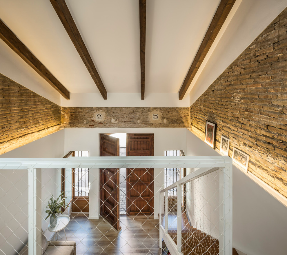 Photo of a medium sized mediterranean mezzanine bedroom in Valencia with brown walls, laminate floors, no fireplace, brown floors, exposed beams and brick walls.