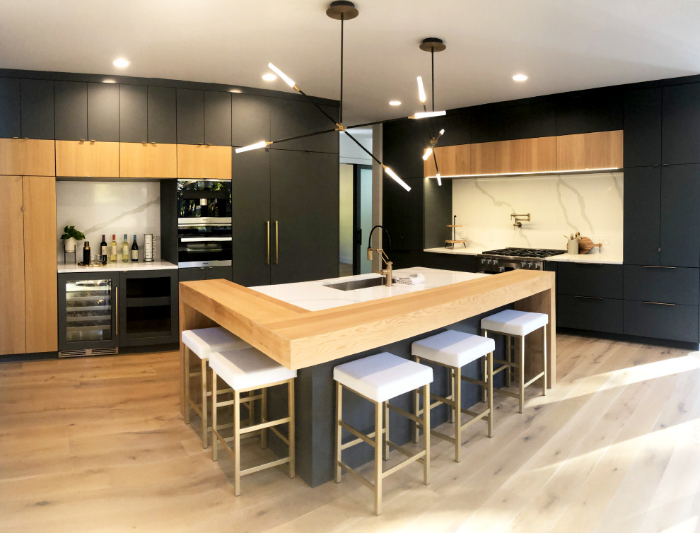 グランドラピッズにある高級な広いコンテンポラリースタイルのおしゃれなキッチン (アンダーカウンターシンク、フラットパネル扉のキャビネット、青いキャビネット、クオーツストーンカウンター、白いキッチンパネル、クオーツストーンのキッチンパネル、シルバーの調理設備、ラミネートの床、ベージュの床、白いキッチンカウンター) の写真