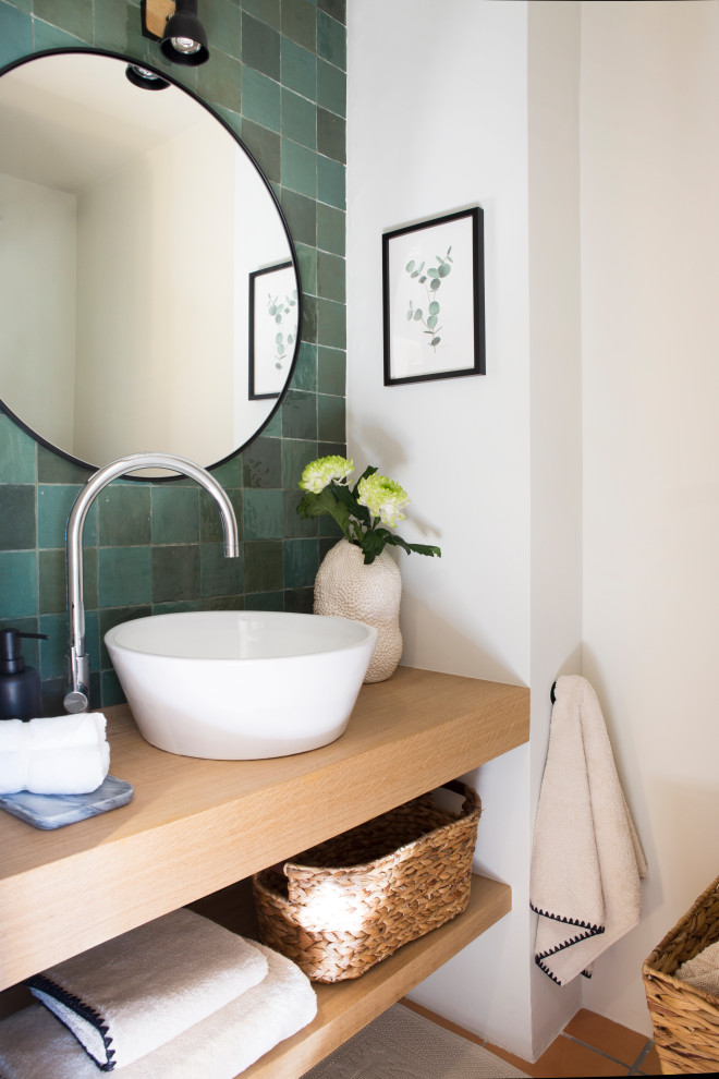 Пример оригинального дизайна: туалет в стиле кантри с белыми фасадами, зеленой плиткой, белыми стенами, полом из терракотовой плитки, настольной раковиной, столешницей из дерева и коричневым полом