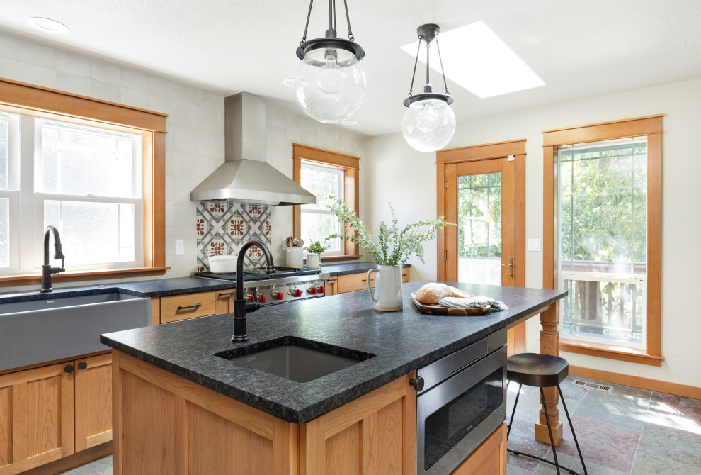 Photo of a mid-sized country u-shaped separate kitchen in Portland with a farmhouse sink, shaker cabinets, medium wood cabinets, granite benchtops, white splashback, ceramic splashback, stainless steel appliances, slate floors, with island, multi-coloured floor and black benchtop.