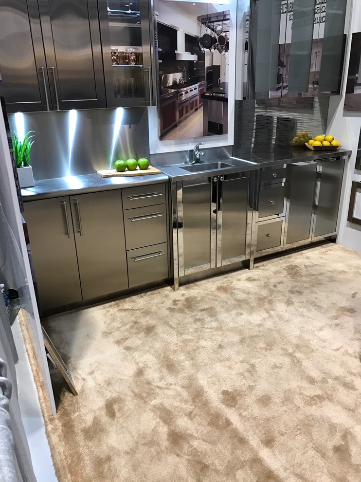 Inspiration for a small contemporary single-wall separate kitchen in New York with an undermount sink, flat-panel cabinets, stainless steel cabinets, stainless steel benchtops, stainless steel appliances, carpet, metallic splashback, metal splashback and brown floor.