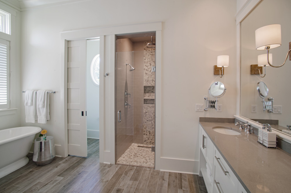 Photo of a beach style master bathroom in Other with shaker cabinets, white cabinets, a freestanding tub, a curbless shower, gray tile, ceramic tile, white walls, ceramic floors, an undermount sink, engineered quartz benchtops, grey floor, a hinged shower door and grey benchtops.