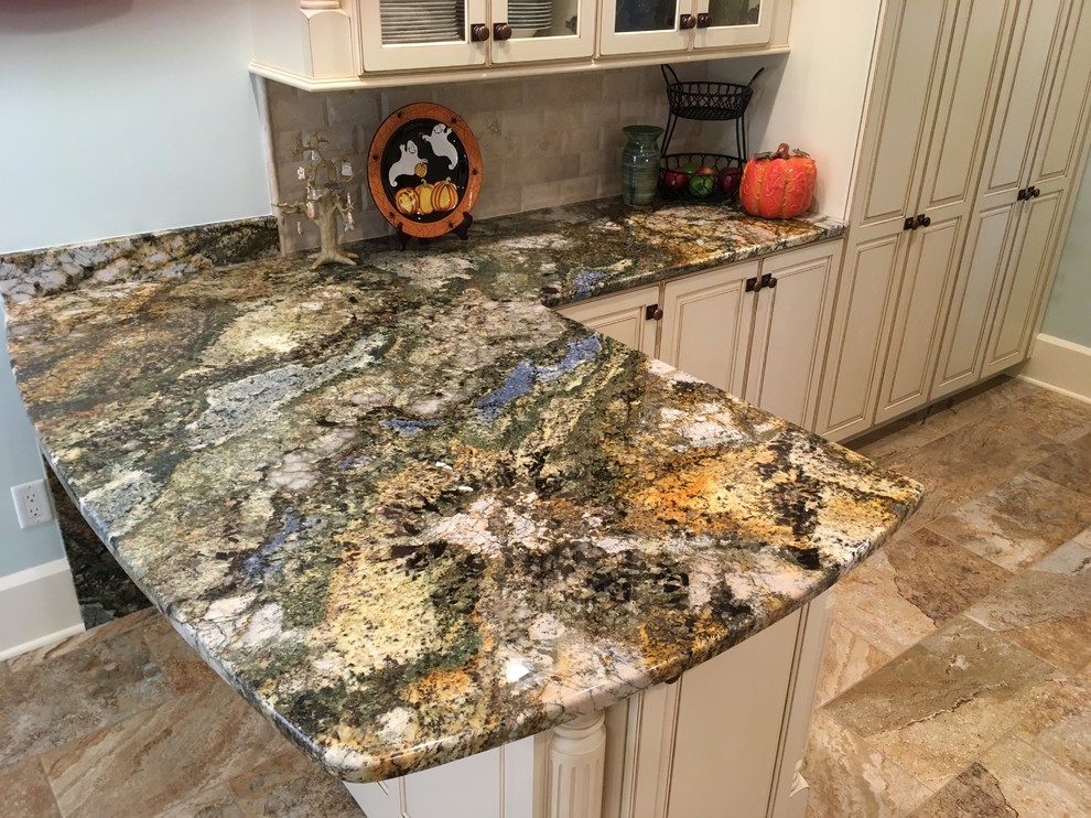 Example of a large transitional galley porcelain tile enclosed kitchen design with an undermount sink, raised-panel cabinets, distressed cabinets, granite countertops, beige backsplash, stone tile backsplash, stainless steel appliances and a peninsula